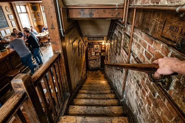 A steep, narrow wooden staircase leading down to a dimly lit pub basement.
