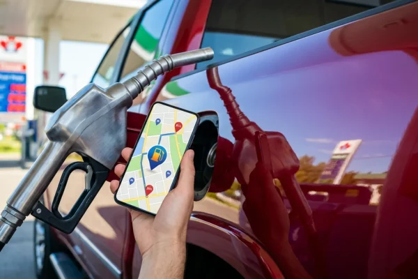 Conducteur souriant utilisant son téléphone près d'une pompe à essence.