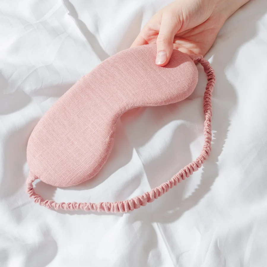 hand holding a pink sleep mask on white sheets.