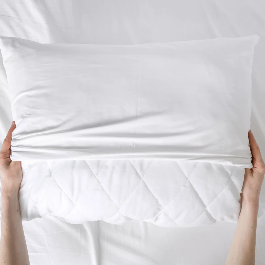 hands holding a white quilted pillow on a bed.