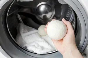 Person placing a white wool dryer ball inside dryer