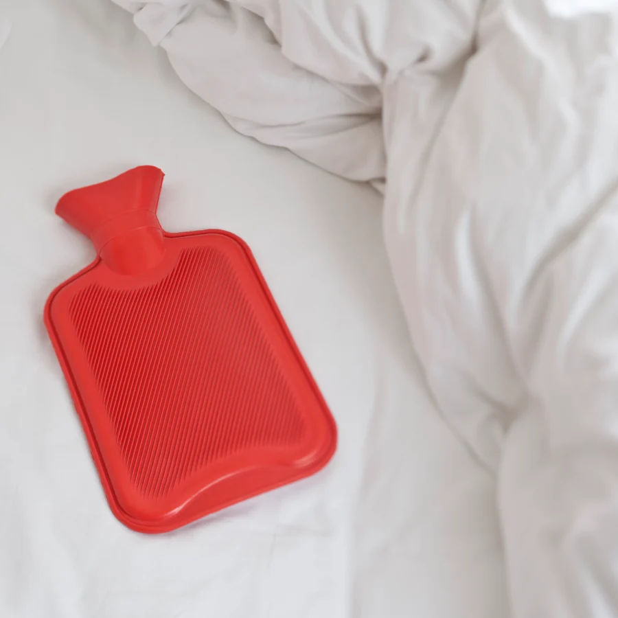 red rubber hot water bottle on white bed sheets.