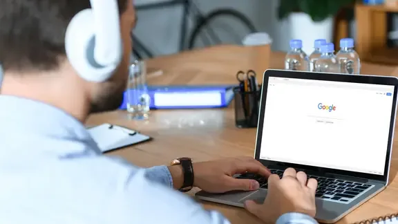 Ein Mann sitzt mit aufgesetzten Kopfhörern vor einem Laptop, der die Website von Google zeigt