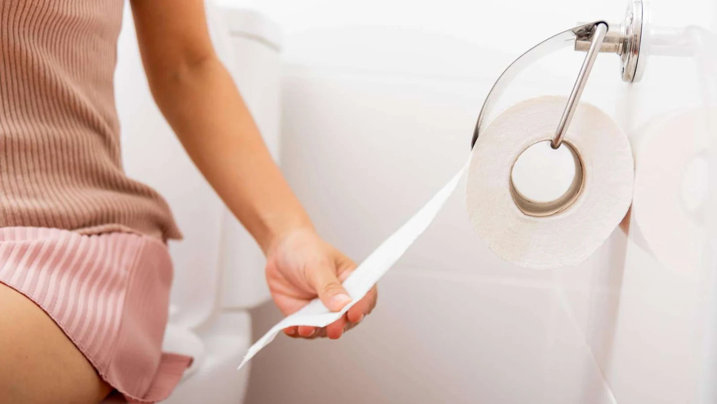 Eine Hand greift eine Rolle Toilettenpapier, die an einem Halter im Bad hängt.