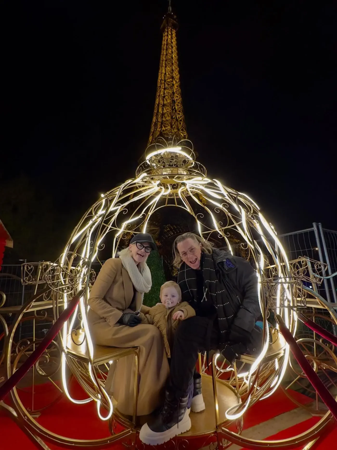 Kelly Osbourne, Sid Wilson, and their baby in a lighted carriage with the Eiffel Tower in the background.