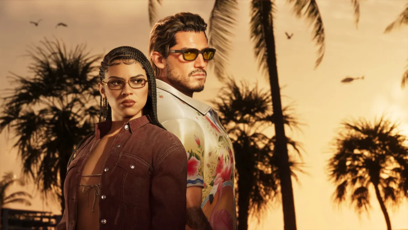 Rockstar Games A screenshot from GTA 6 shows main characters Lucia and Jason standing back-to-back against a palm tree-lined sunset. She wears tinted glasses, her long dark hair styled in side-parted cornrows. She wears a tan suede jacket over a string bikini top. He also wears tinted shades and a white shirt with an oversized collar and floral pattern.