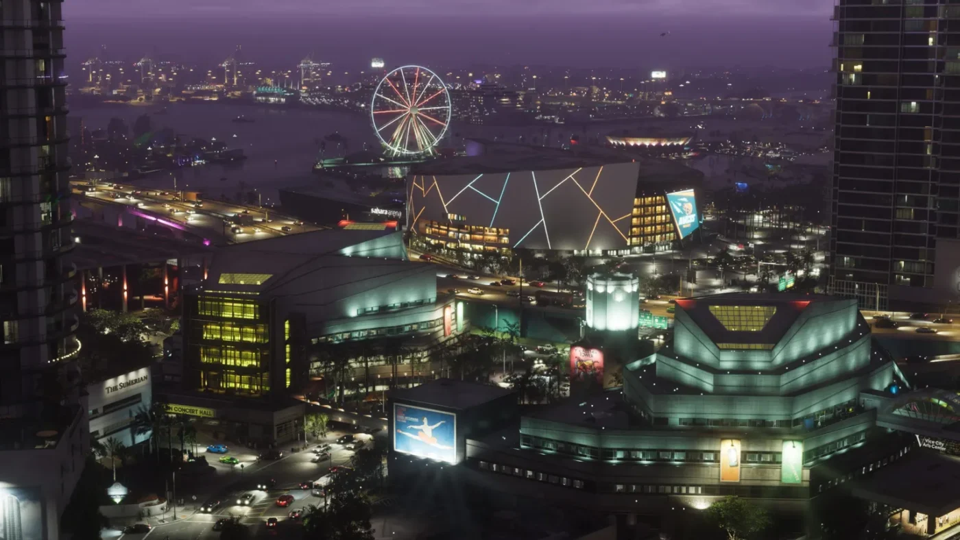 Rockstar Games An aerial screenshot shows downtown Vice City at night. Blocks of apartments, a stadium with a large animated billboard and an illuminated Ferris wheel create a glowing tapestry of colours. In the distance, on the other side of a port, the lights of more buildings dot the skyline.